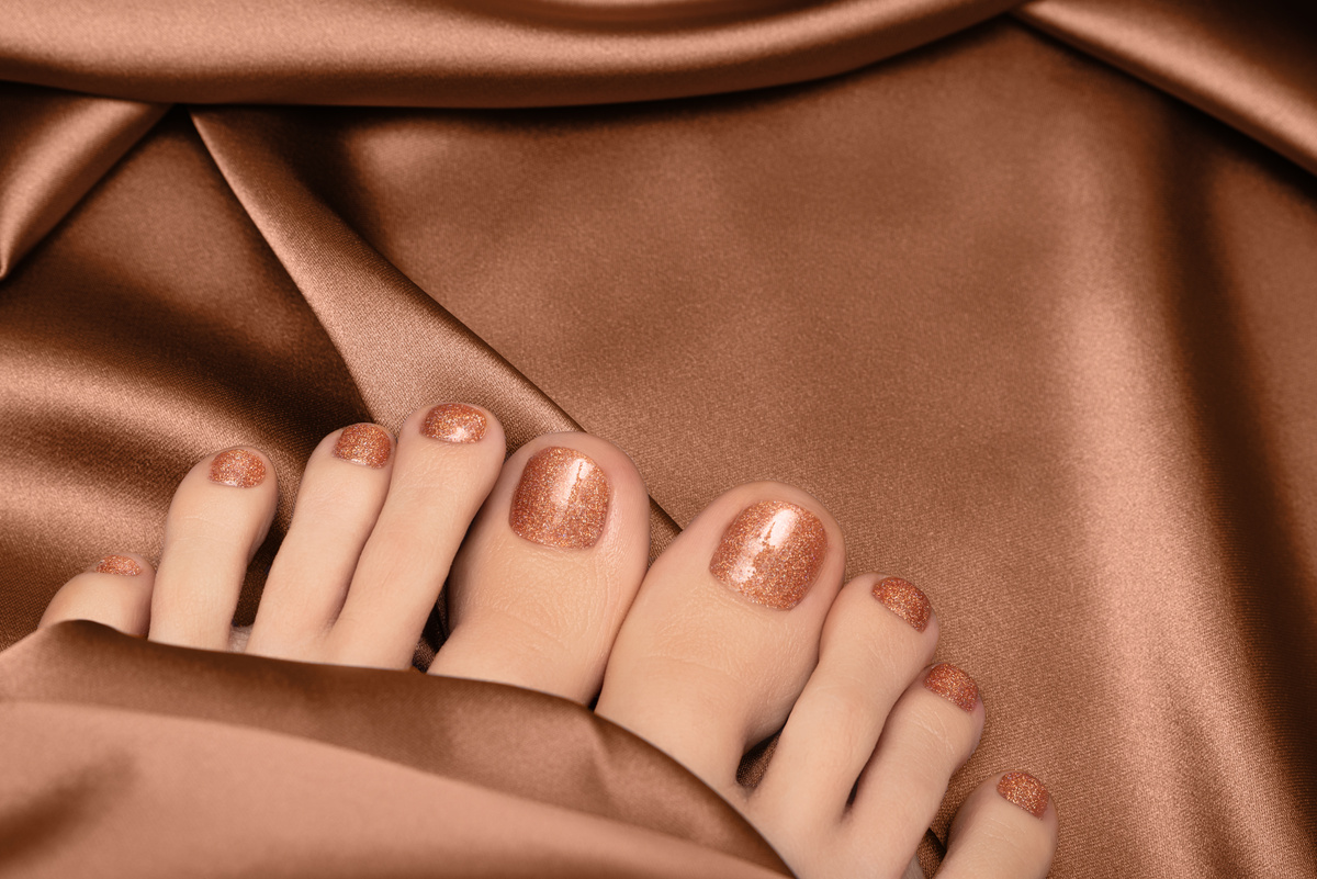 Female feet with bronze nail design. Glitter bronze nail polish pedicure with nail art. Woman feet on fabric background.